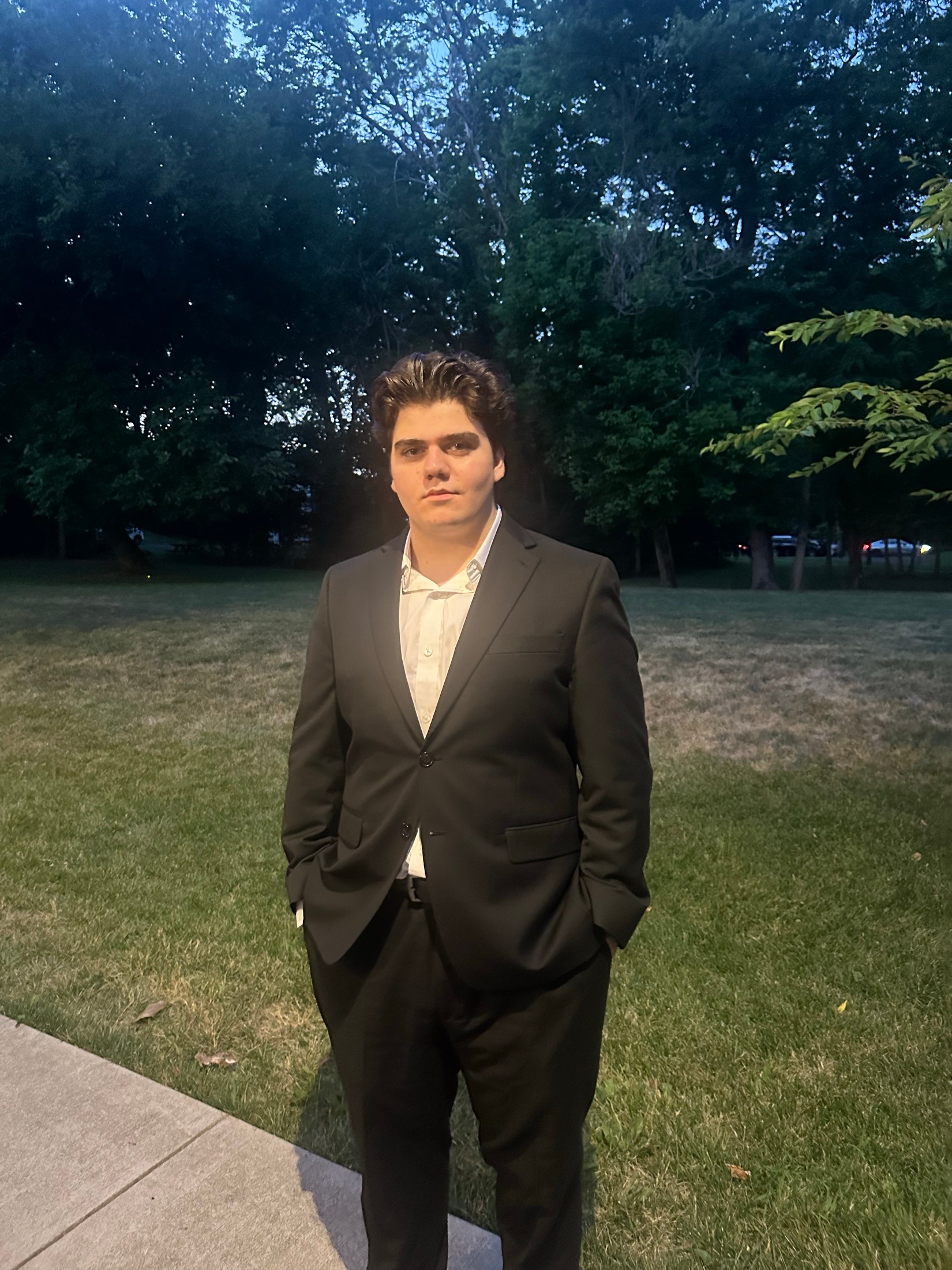 Ertuğrul Ertan in a charcoal suit, standing outdoors among trees